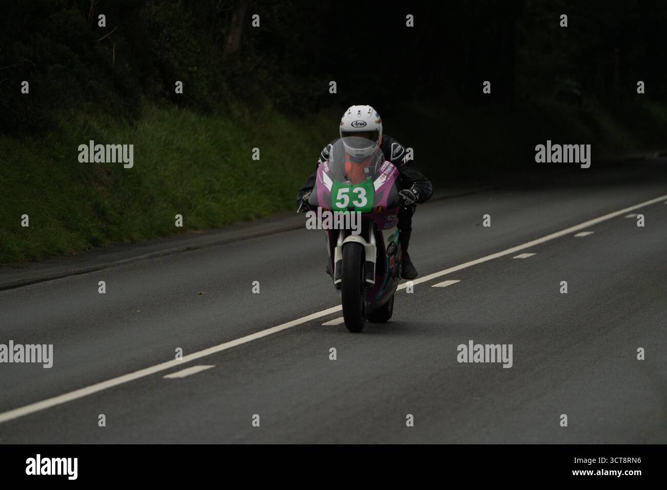 Racing motorcyclist number 53 on Isle of Man road circuit with pink and ...