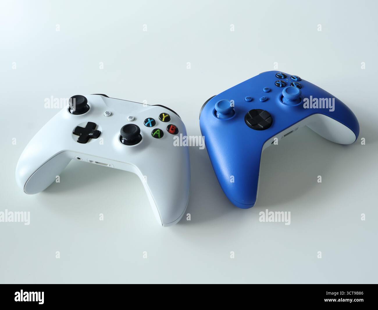Two modern game controllers, white and blue, rest on a clean, pale surface. Ideal stock imagery for gaming, accessories, and entertainment topics Stock Photo