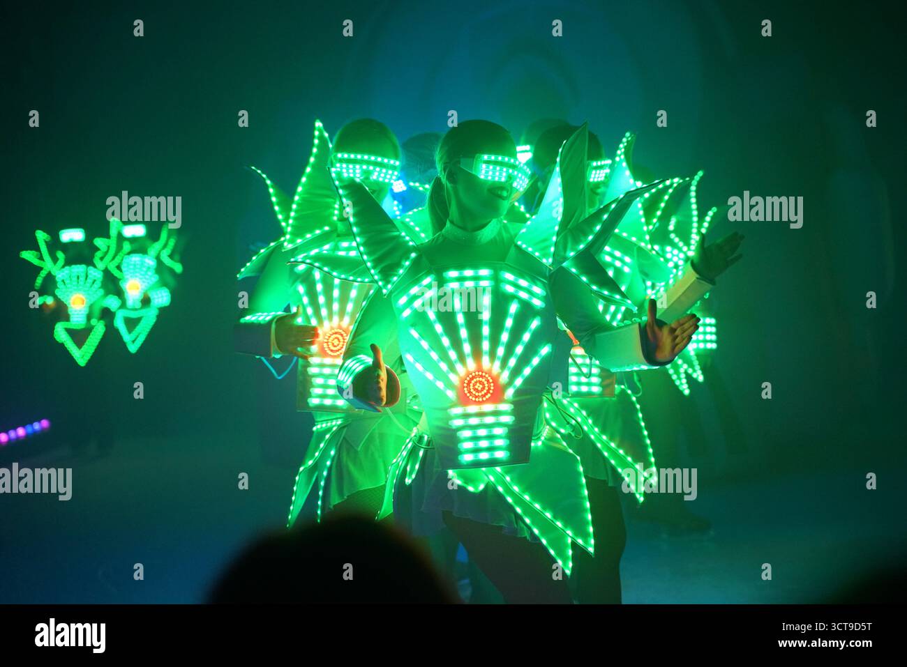 Brightly lit performers showcase neon costumes during an electrifying dance routine in a vibrant venue Stock Photo