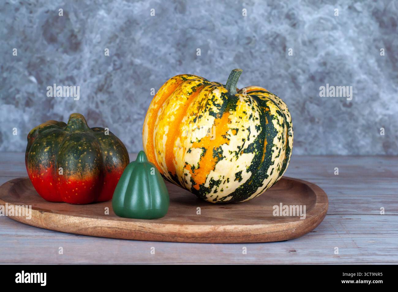 A pumpkin sits on a wooden tray next to a green squash Stock Photo