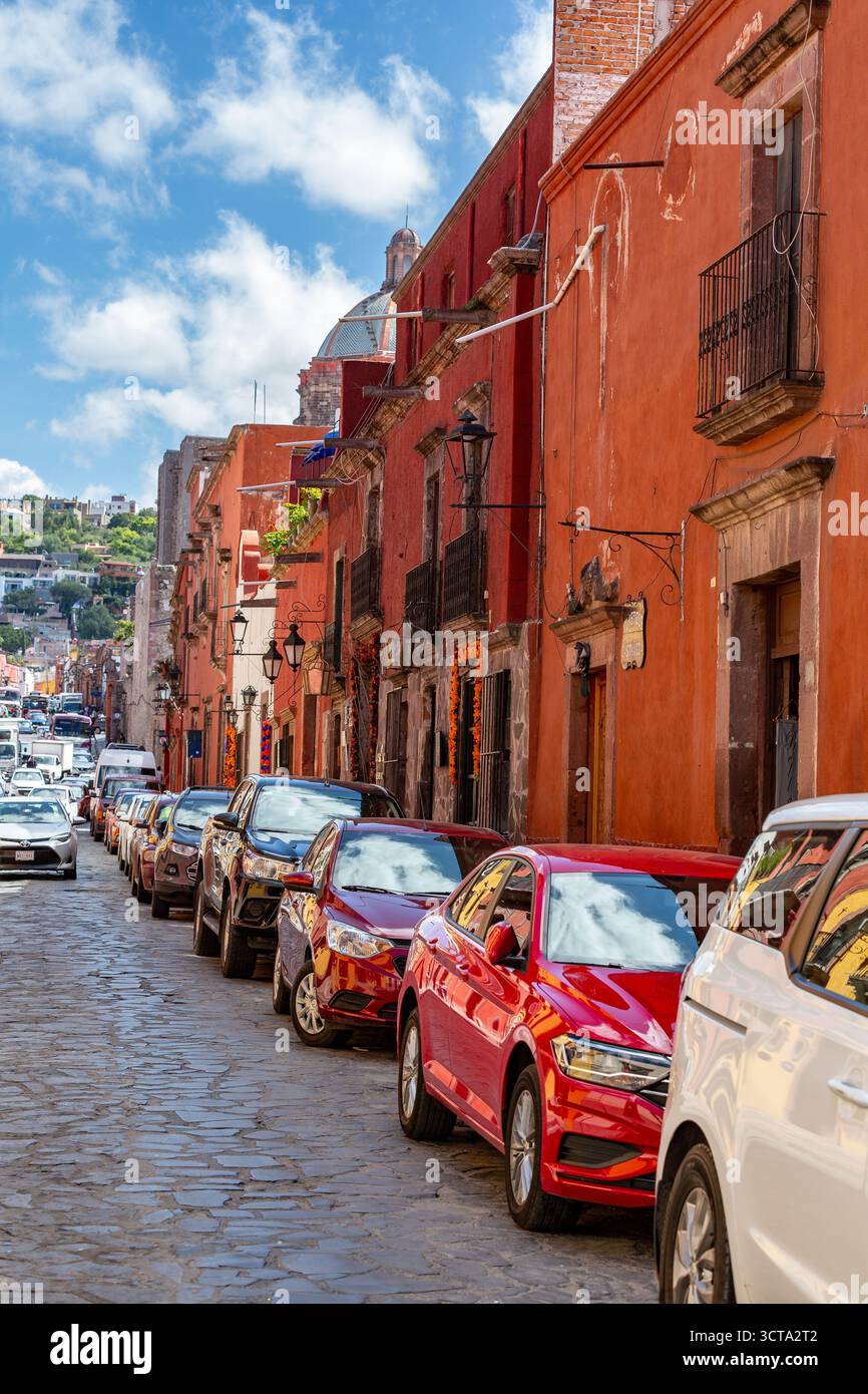 Cars are parked along a cobblestone street in front of red buildings in ...