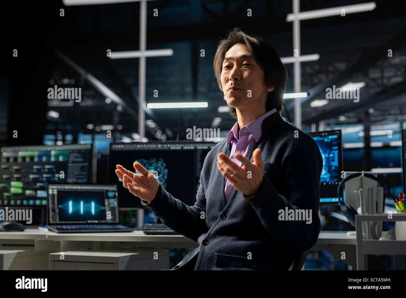 Computer scientist in server room using device to review infrastructure diagnostics. Asian senior programmer in high tech data center analyzing performance data to maintain system uptime Stock Photo