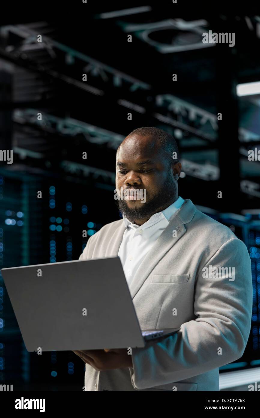 Server hub developer using laptop to fix network issues affecting storage arrays, doing backups. Programmer in data center runs system diagnostic tests, scanning hardware logs for faults Stock Photo