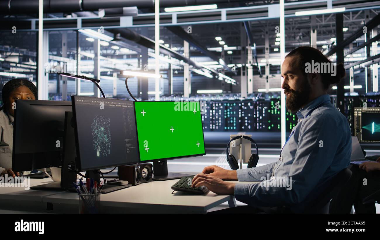 Engineer using green screen mockup PC in data center to update servers tech, configuring equipment using software tools. Server room worker reviewing hardware analytics on chroma key PC, camera A Stock Photo