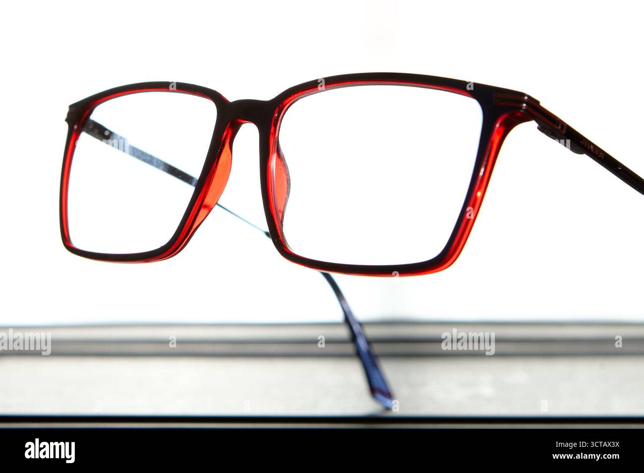 Macro closeup of red eyeglasses frame isolated on white background with reflection, representing eyewear design, optical care and fashion accessory co Stock Photo