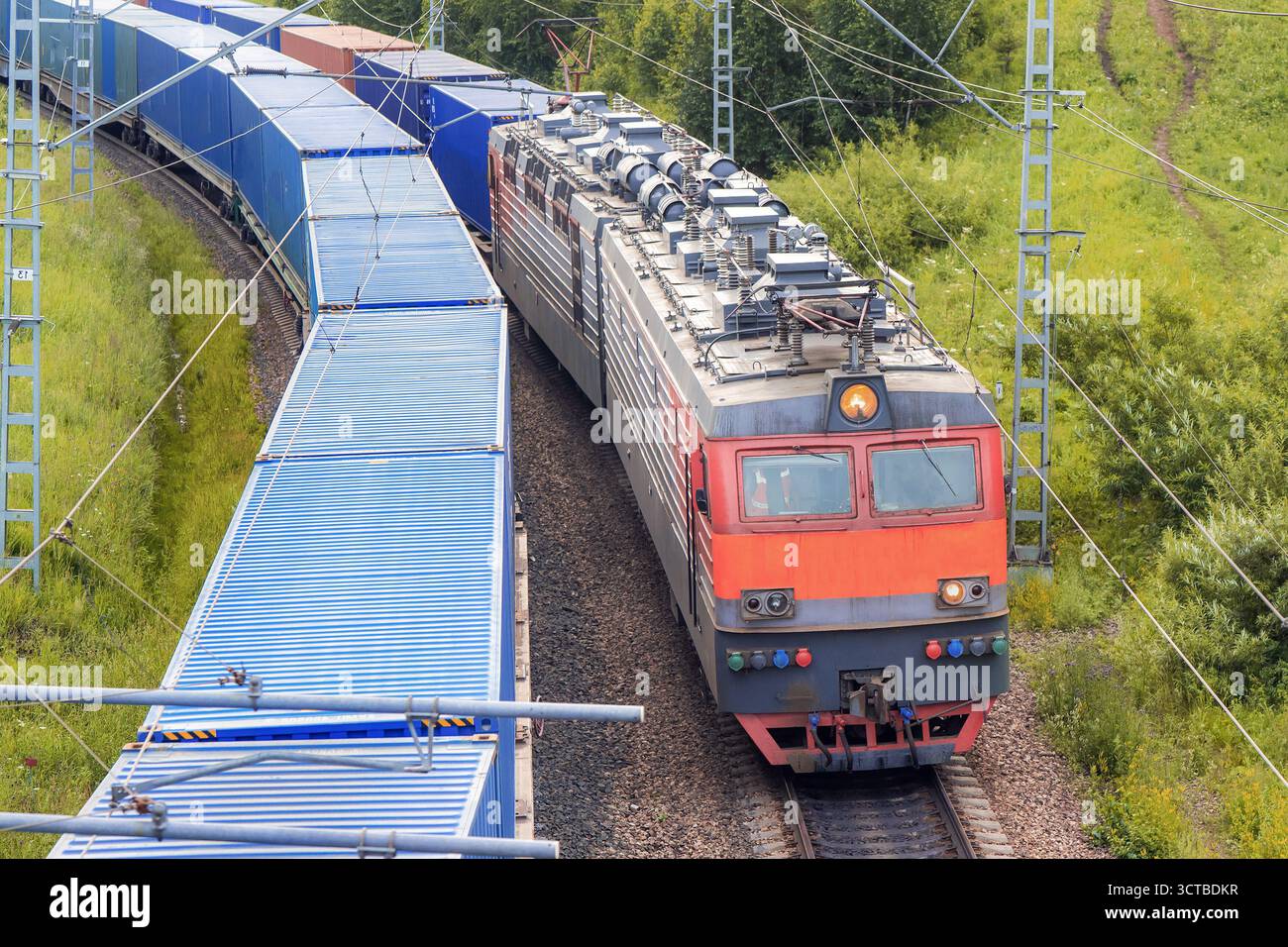 Parallel Train A red railway locomotive train with shipping containers rides next to a ...