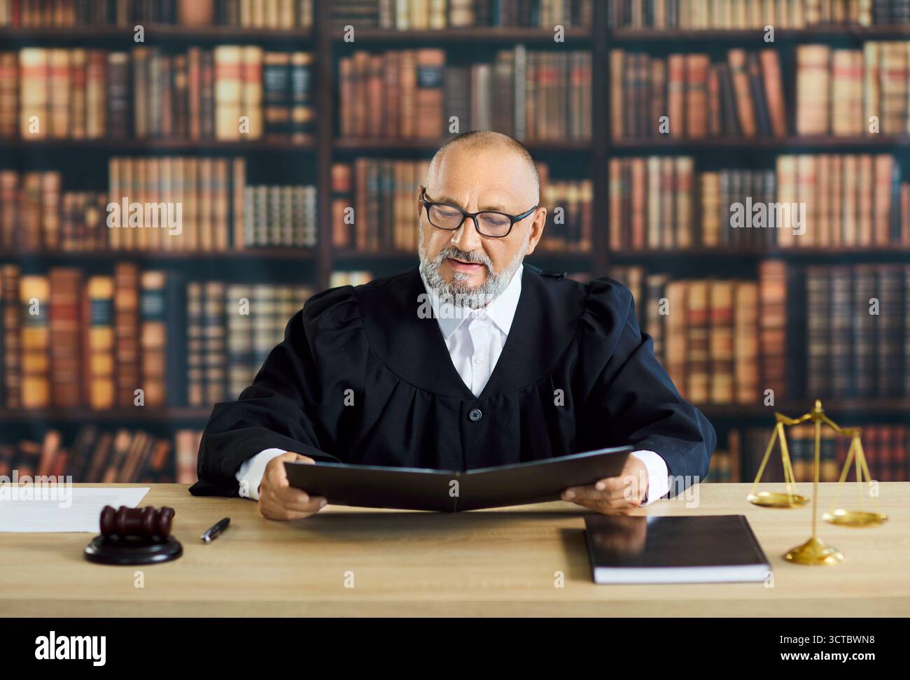 Reading Case File Senior judge reading case file at desk, gavel and scales in law library ...