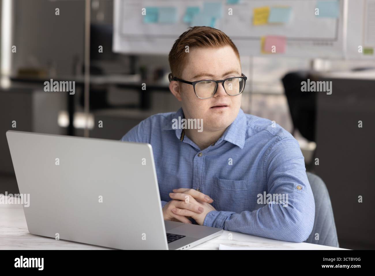 Thoughtful young professional man with Down syndrome working at laptop Stock Photo