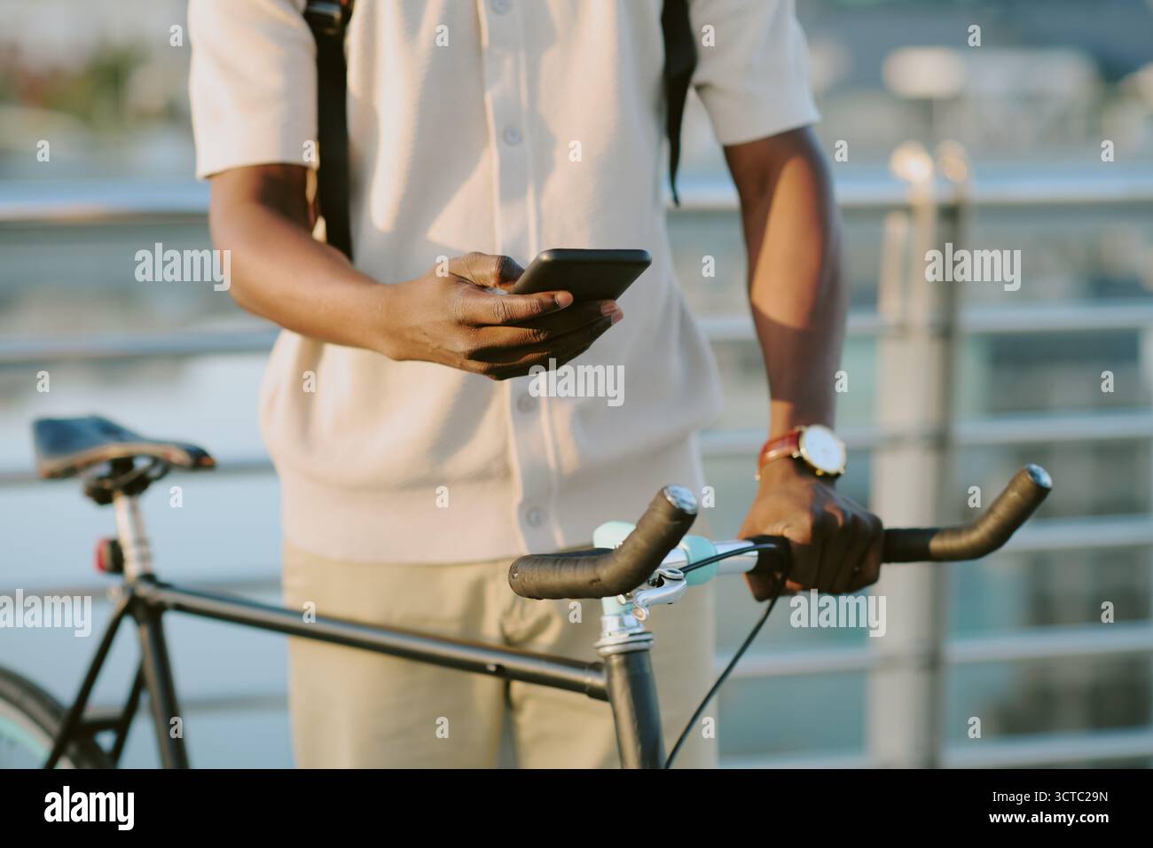 Young Adult Black Man Using Smartphone While Standing Beside Bicycle Outdoors Stock Photo