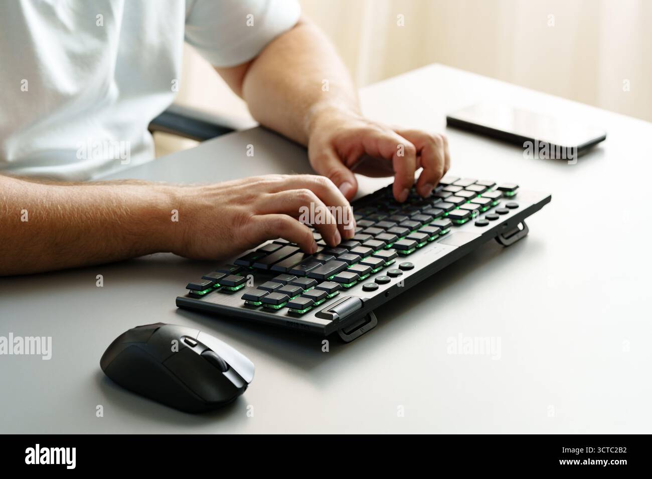 Typing on a modern keyboard while using a computer mouse in a bright office setting Stock Photo