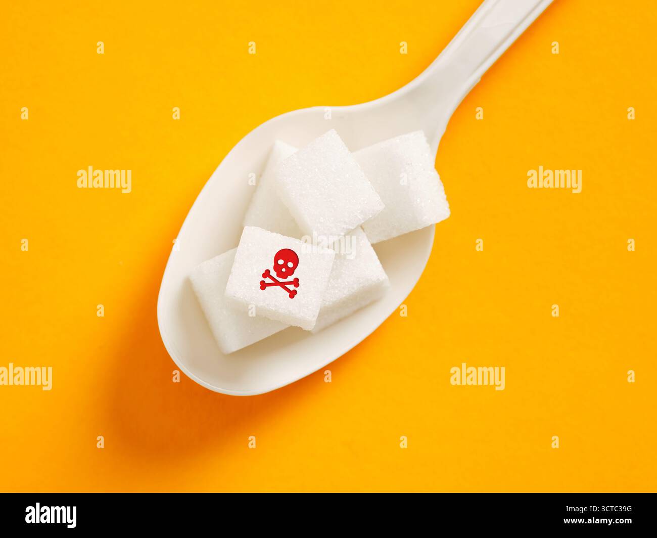 Sugar cubes with a skull and crossbones symbol on a white spoon, representing the danger and unhealthy aspects of sugar consumption Stock Photo