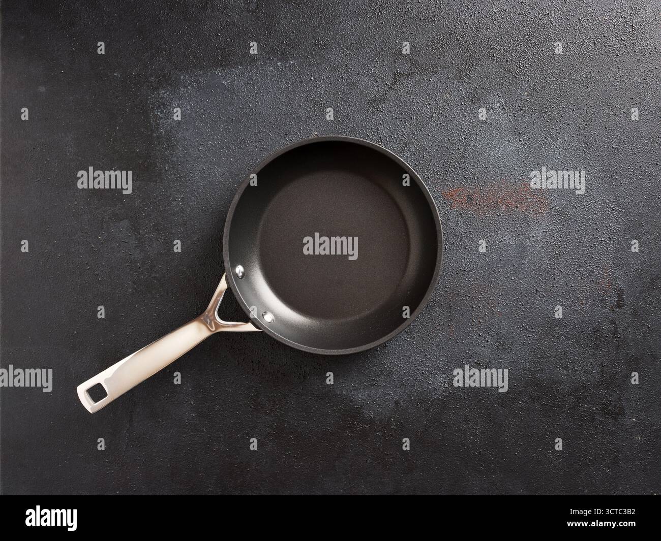 Empty frying pan featuring a non-stick surface and stainless steel handle, positioned on a textured dark gray cooking surface Stock Photo