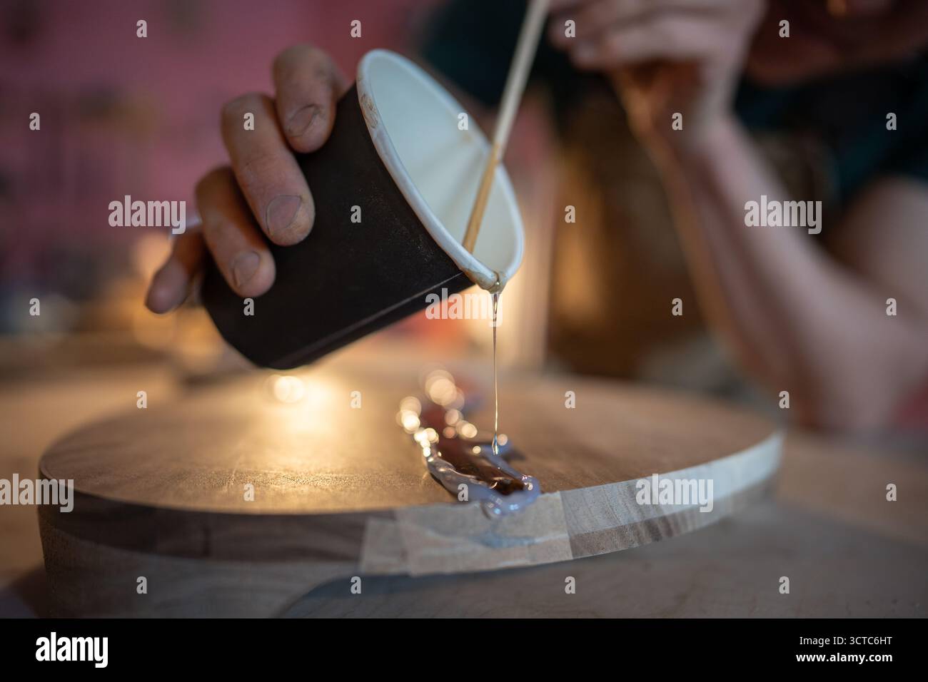 Craftsman pouring epoxy resin into crack on wood surface using stick ...