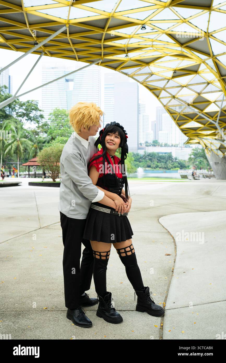 Cosplayers are hugging each other under an elaborate yellow metal structure in an urban setting Stock Photo