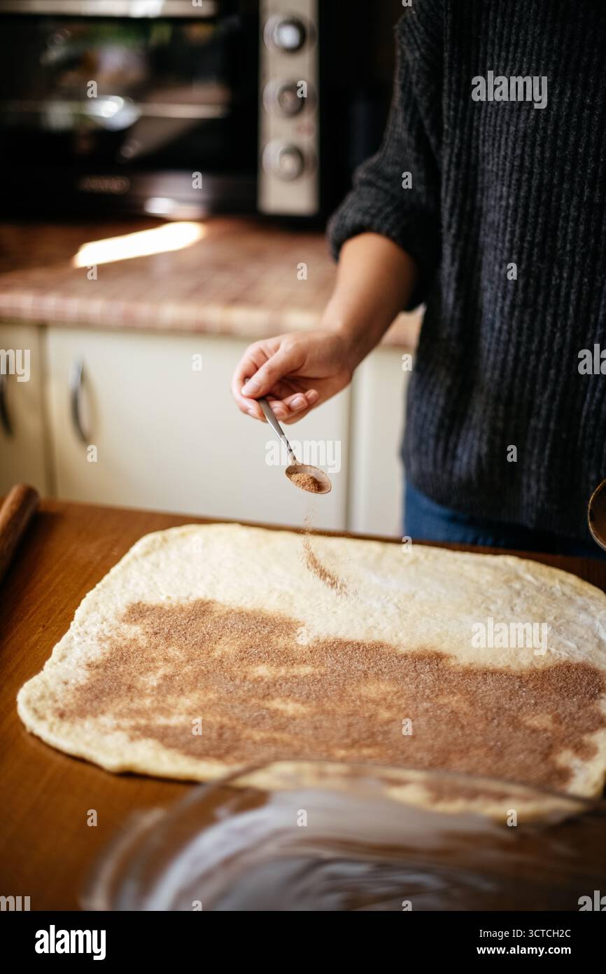 Sprinkling cinnamon on rolled dough Stock Photo