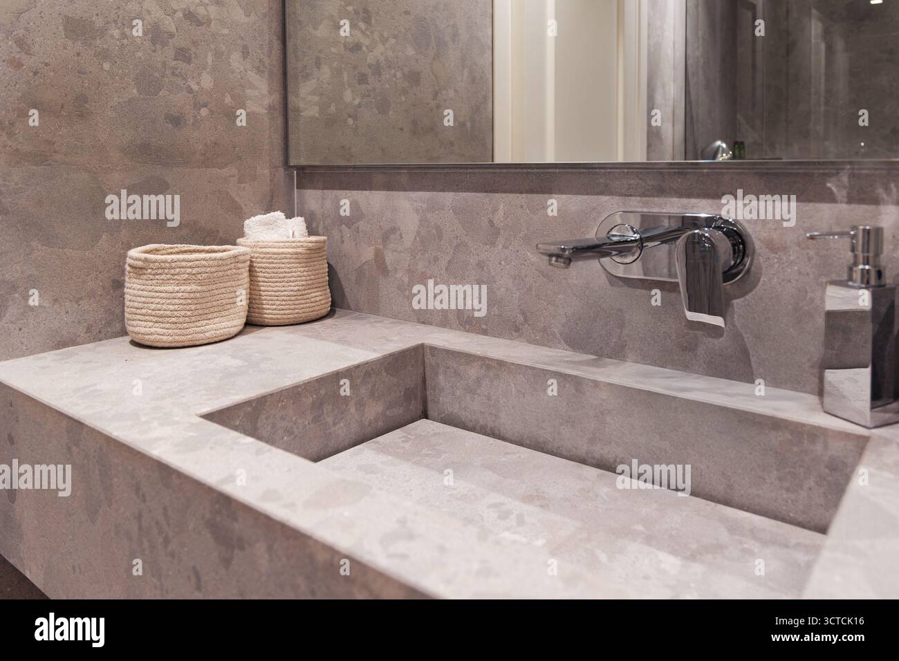 Modern bathroom vanity featuring a natural stone basin, wood shelf, and a mirror. A hair dryer hangs nearby, suggesting full amenities Stock Photo
