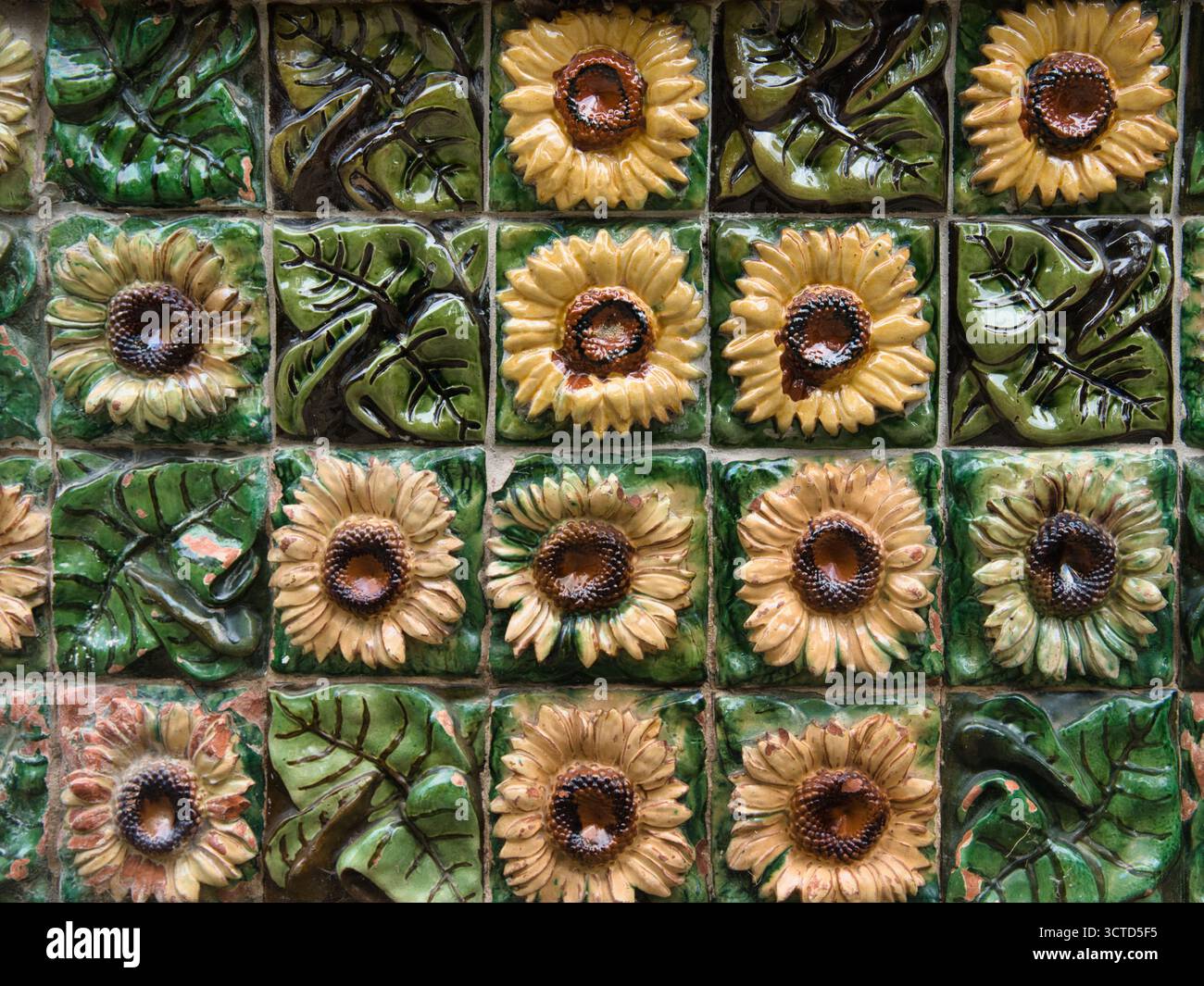 Glazed Ceramic Sunflower Detail Close-up - Macro view of decorative, handcrafted ceramic tile border featuring glossy green leaves and beige sunflower Stock Photo