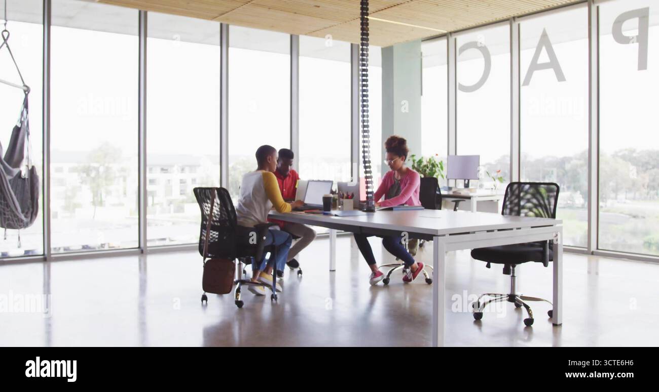 Collaborating three office workers using laptops in open-plan office, with hammock and coffee mugs Stock Photo