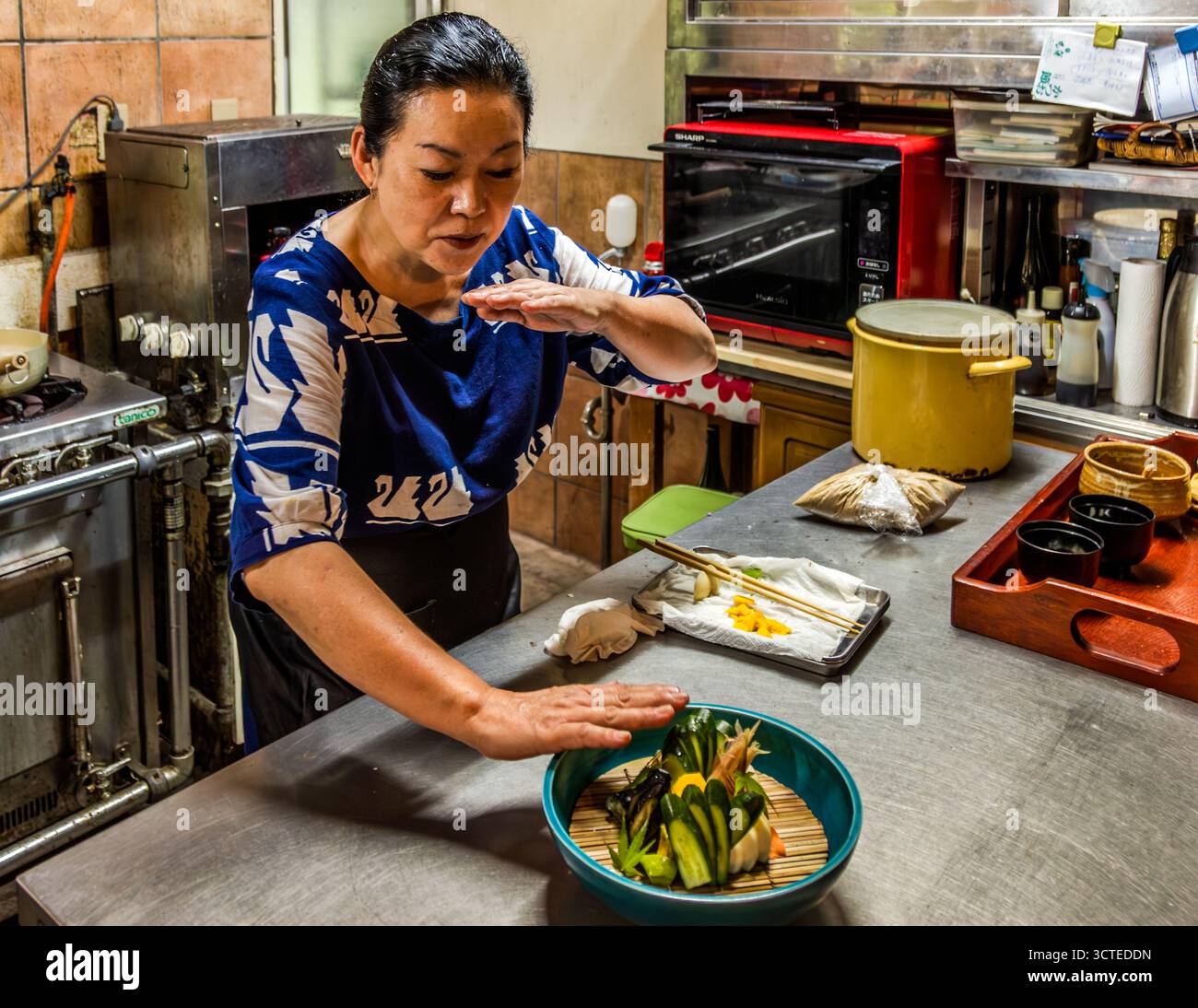 Rakan, a kaiseki restaurant run by chef Atsuko Kato, on the Izu Peninsula, Japan. Atsuko Kato explains the rules of moritsuke, the Japanese art of plating, to travel journalist Angela Berg while scooping rice from a wooden rice tub. They are a complex blend of aesthetics and practical functionality, aimed at giving dishes a harmonious, natural and inviting presentation. Izu, Japan Stock Photo