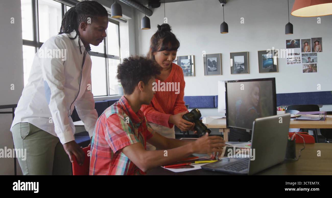 Collaborating colleagues exchanging DSLR camera and reviewing printed layouts at creative workspace Stock Photo