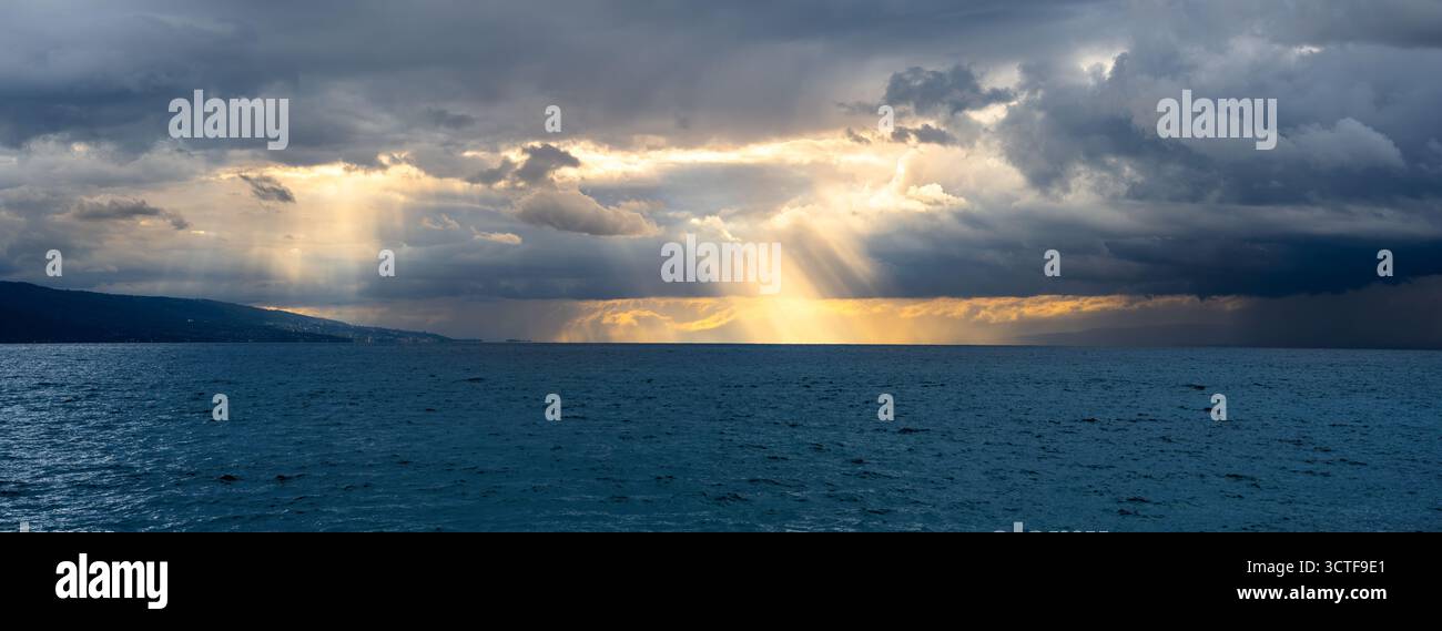 Dramatic horizon on Geneva lake with sun rays breaking through dark clouds. Stock Photo