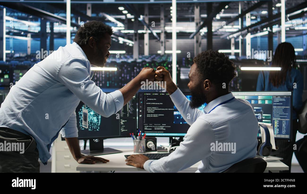 Server hub manager checking AI generated data analytics graphs, congratulating worker. Data center team leader doing fist bump with admin using artificial intelligence showing system metrics, camera A Stock Photo