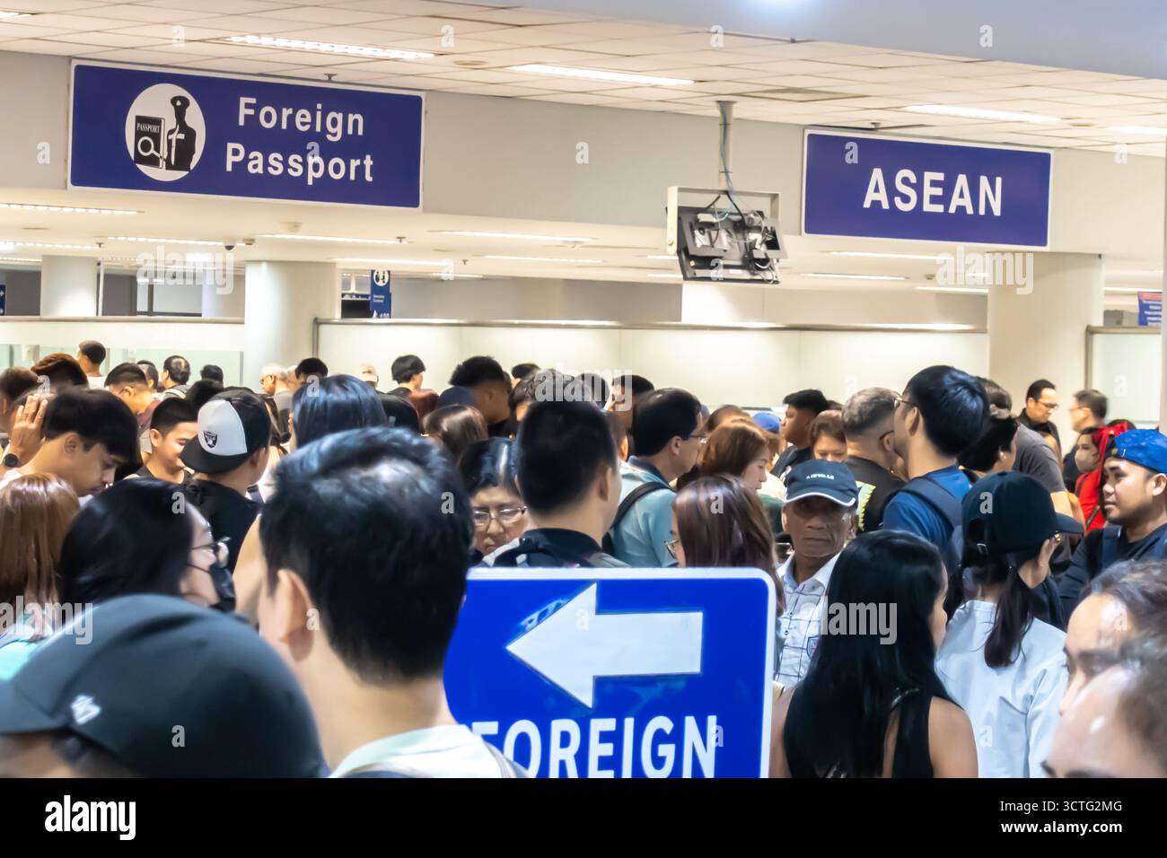 Crowded area in airport, travelers waiting in line, signs for Foreign Passport and ASEAN at the departures terminal in Manila Airport, Philippines Stock Photo