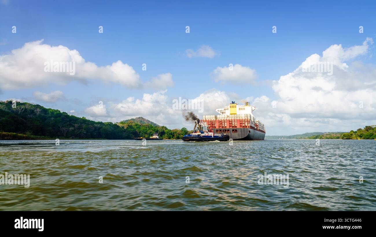 Tug boat accompanying a container ship traveling down Panama Canal Stock Photo