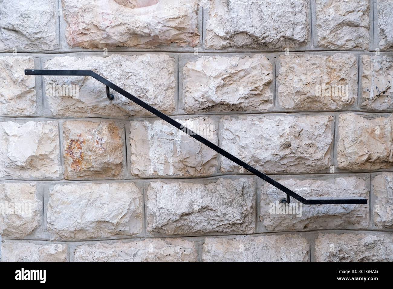 Iron Railing on Textured Stone Wall Surface. High quality photoSimple black iron handrail mounted on a rugged light beige stone wall. Clean architectural detail with texture and contrast,  Stock Photo
