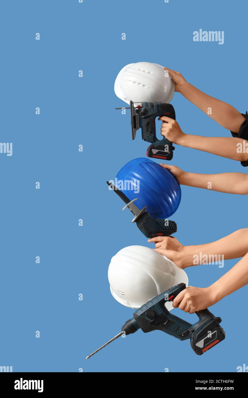 Hands with hardhats and construction tools on blue background Stock Photo