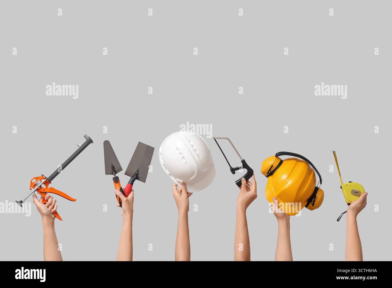 Hands with hardhats and construction tools on grey background Stock Photo