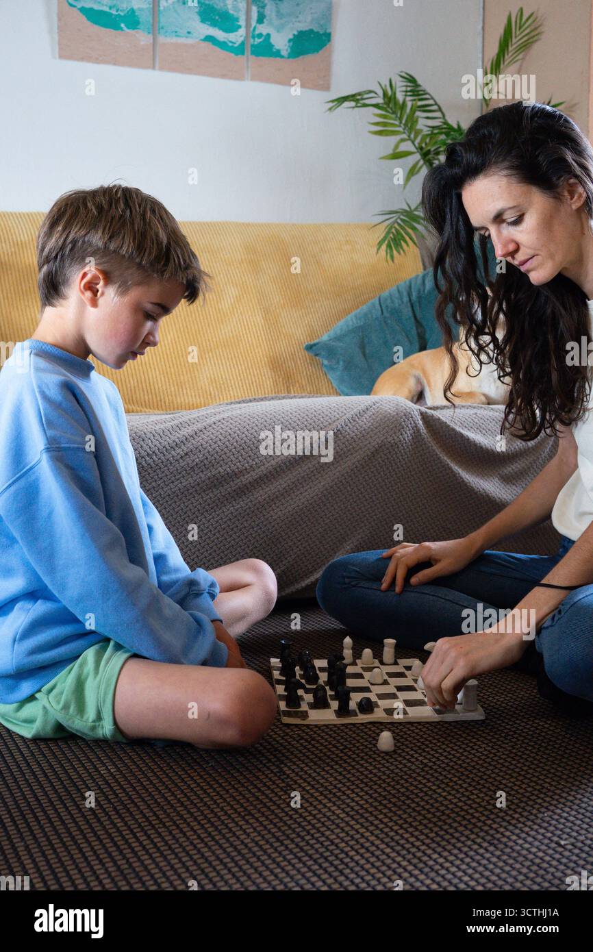 Mother and son sitting on the floor focusing on their next chess moves in the living room Stock Photo
