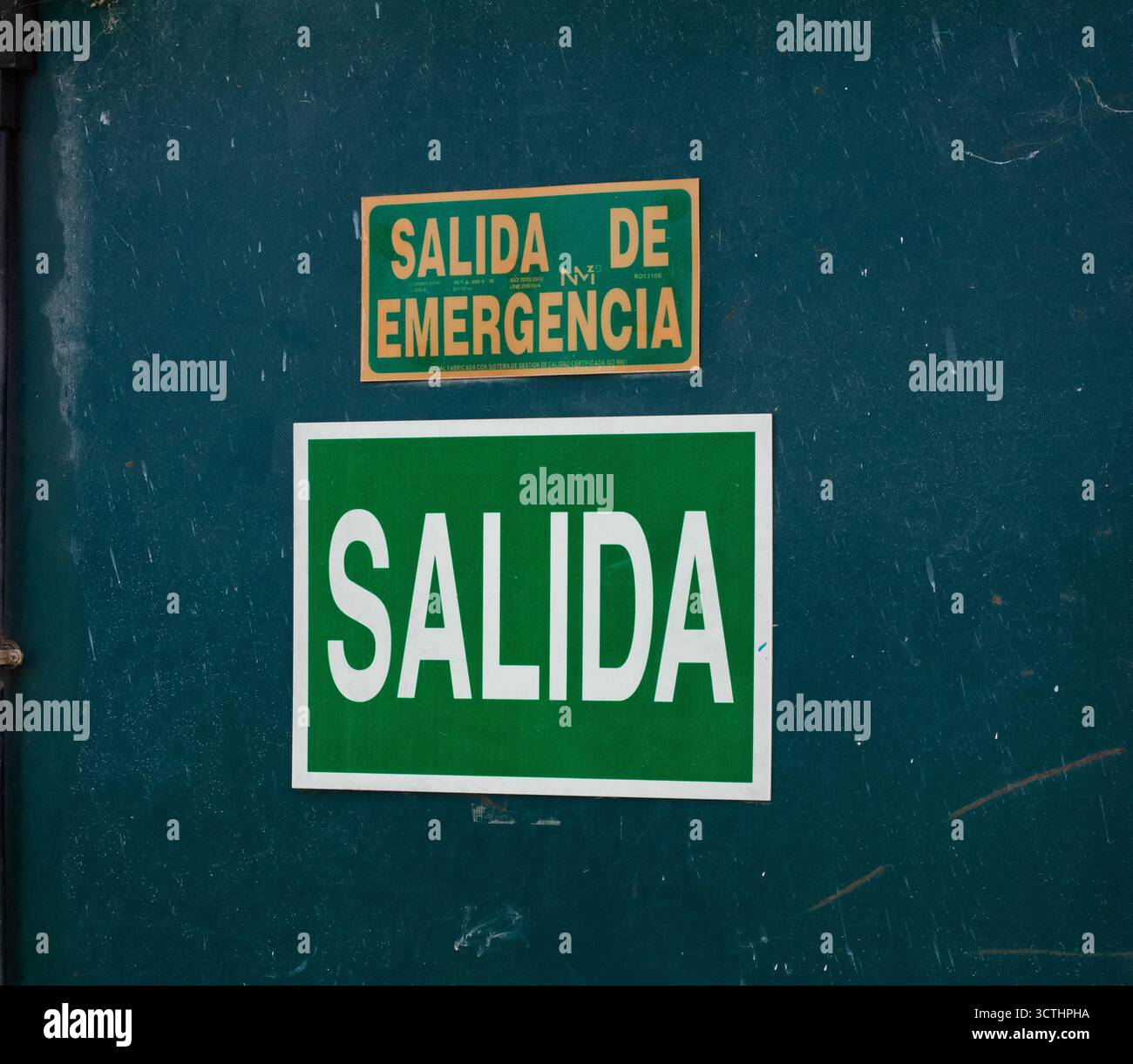Green exit and exit de emergency signs on a dark green metal door, indicating a pathway to safety Stock Photo