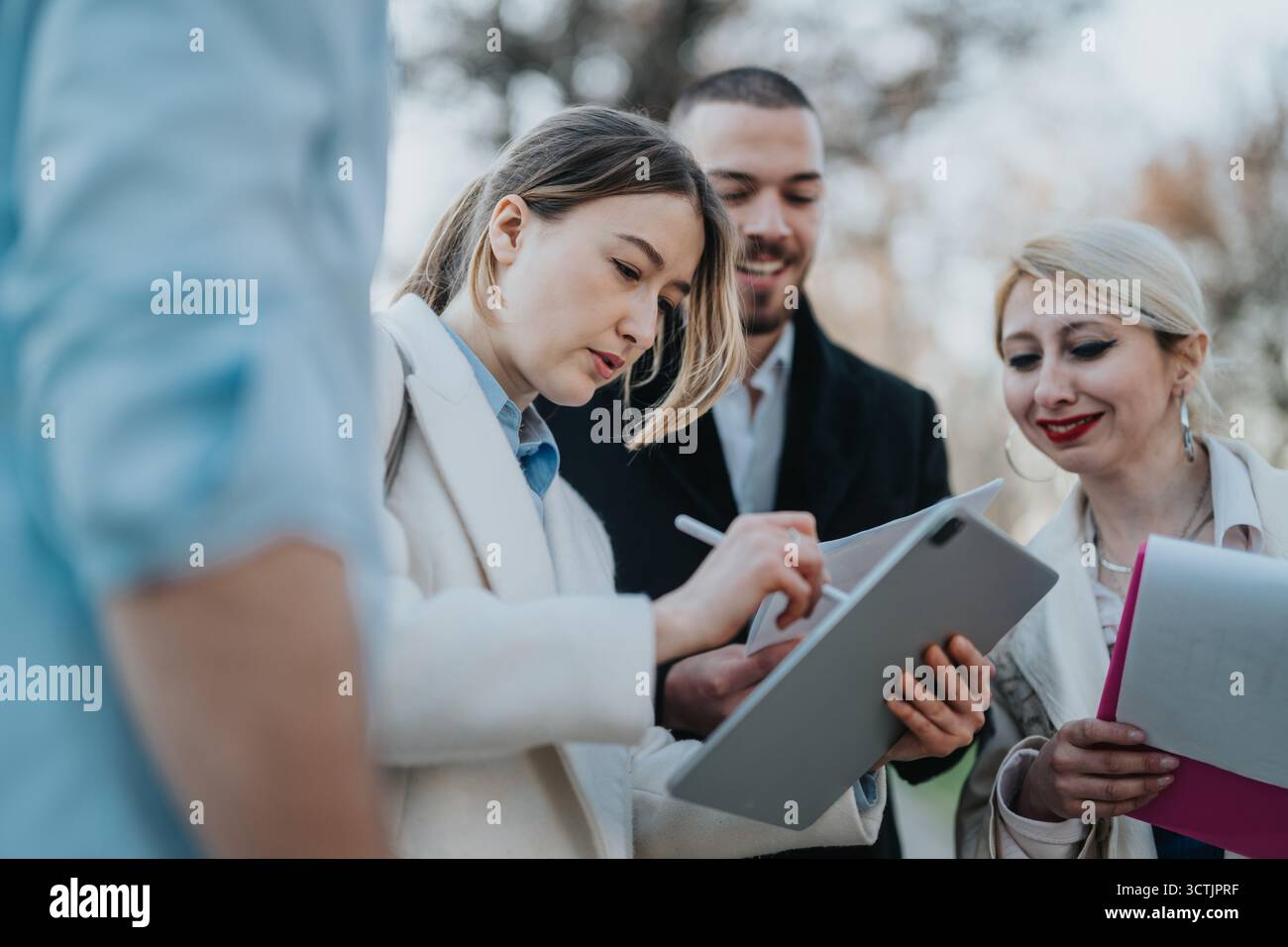 Colleagues collaborating on a project outdoors using digital devices and documents. Stock Photo