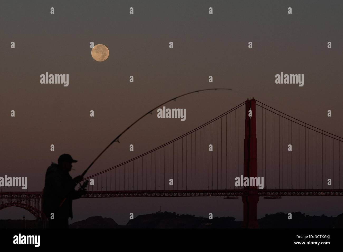 A man fishes as the Harvest Supermoon begins to set over the Golden ...