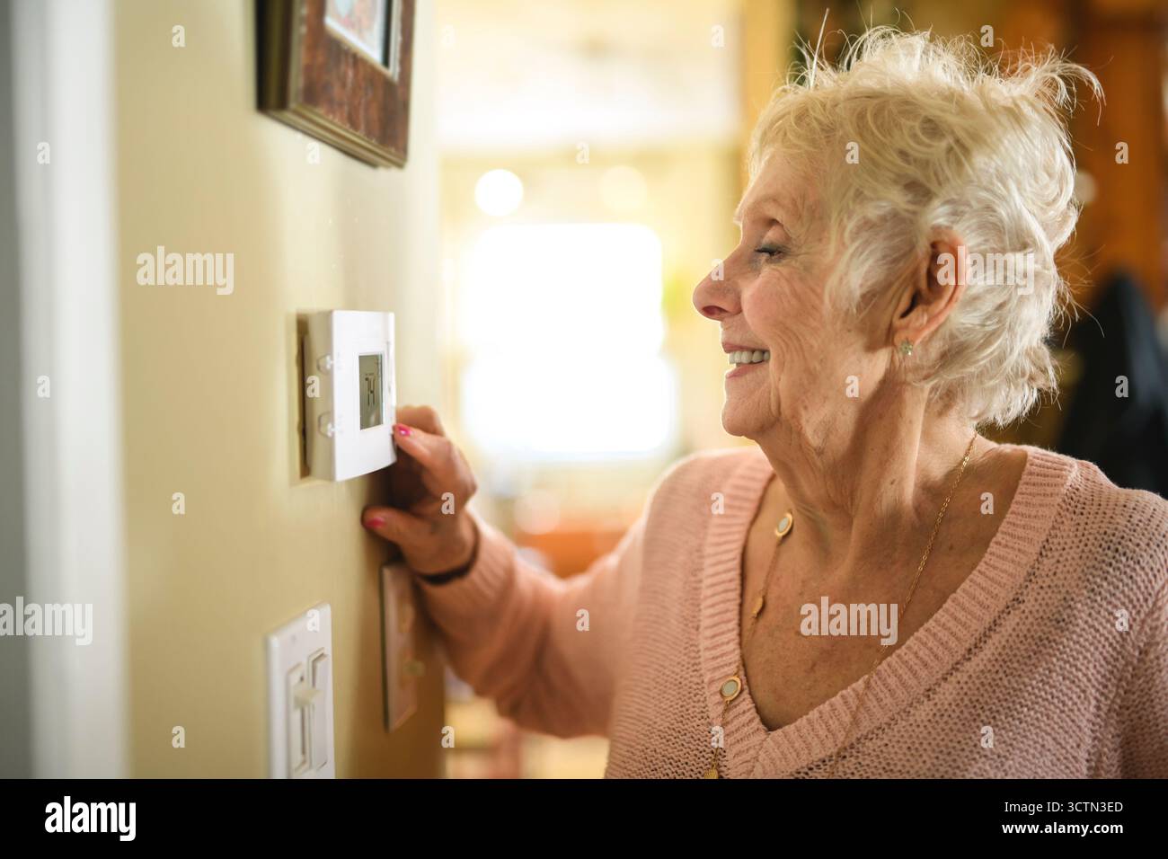 senior lady posing at home portrait close to a window using thermostat Stock Photo