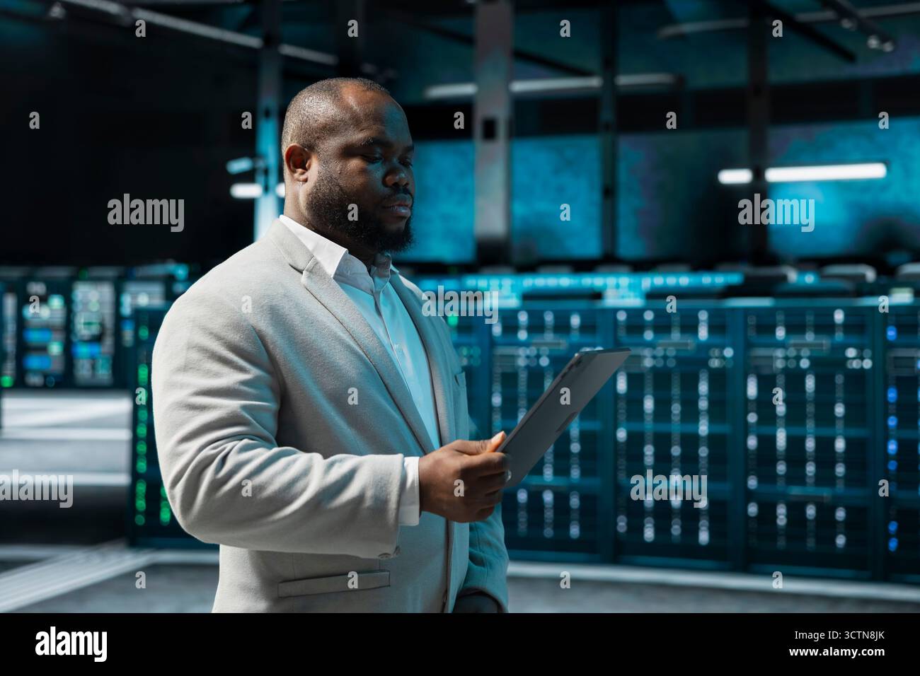 Programmer in data center updating systems using tablet, debugging app performance issues. Server hub IT expert using device, looking for malfunctions, increasing maximum efficiency and uptime Stock Photo