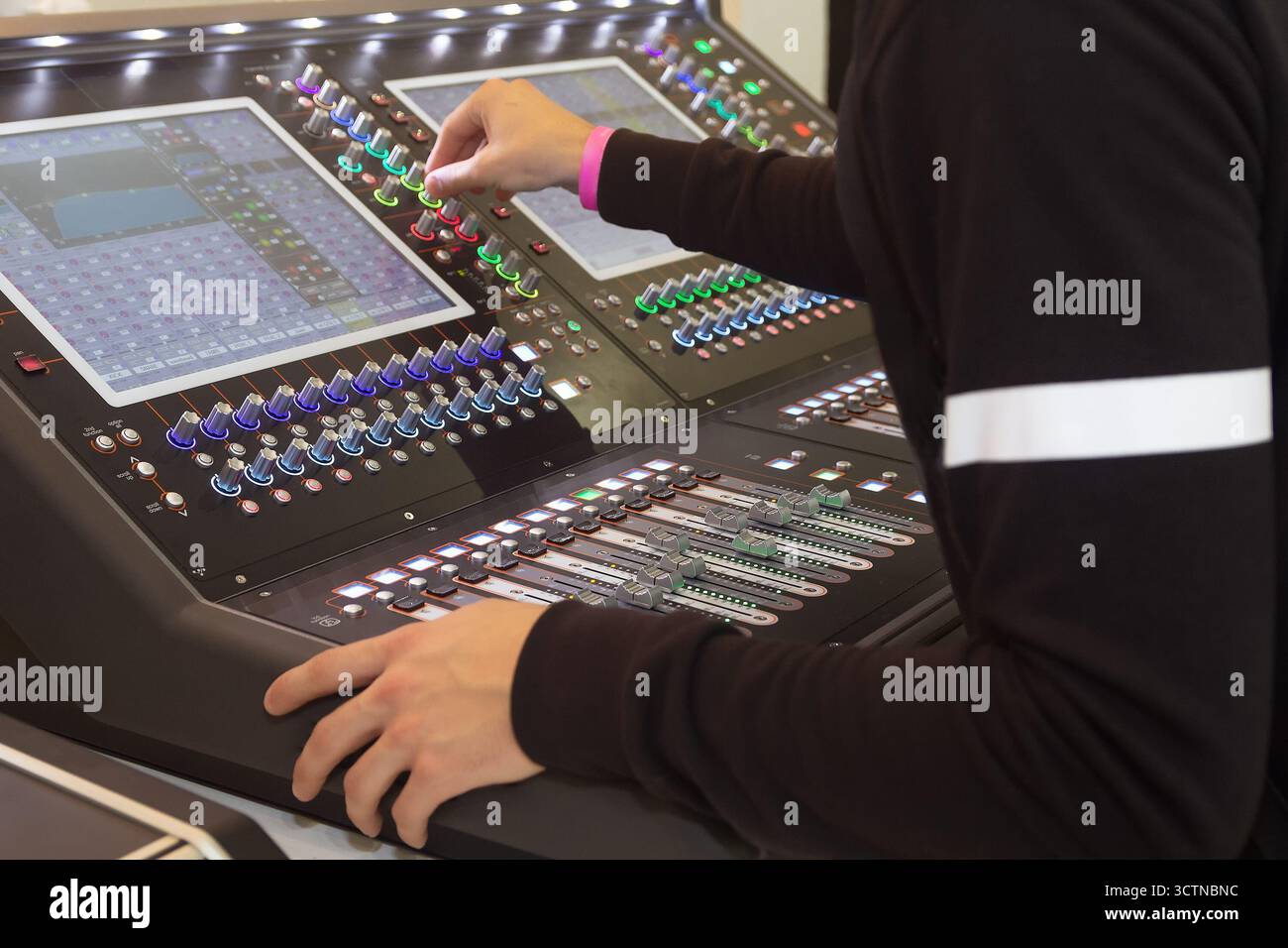 Sound engineer's hand on a professional audio mixing console. Technician adjusting fader in a broadcast control room. Stock Photo