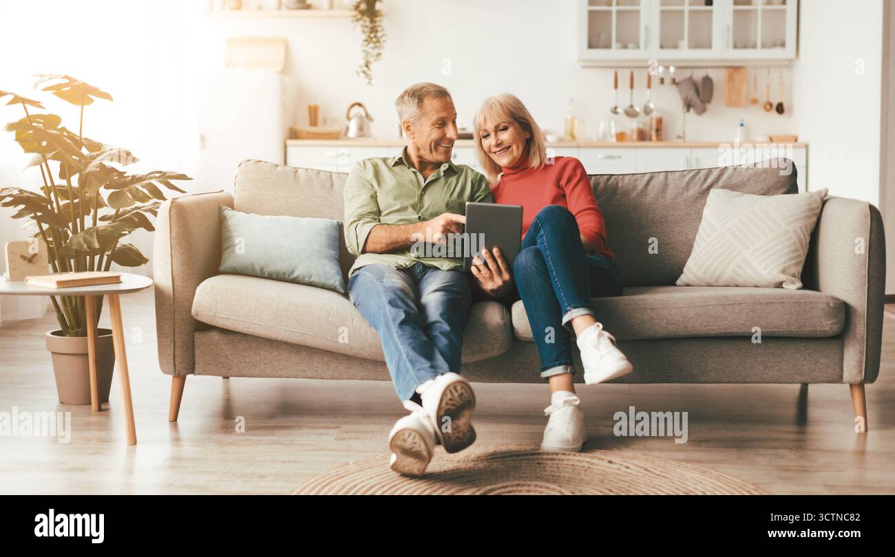 Cheerful Mature Spouses Using Digital Tablet At Home Stock Photo