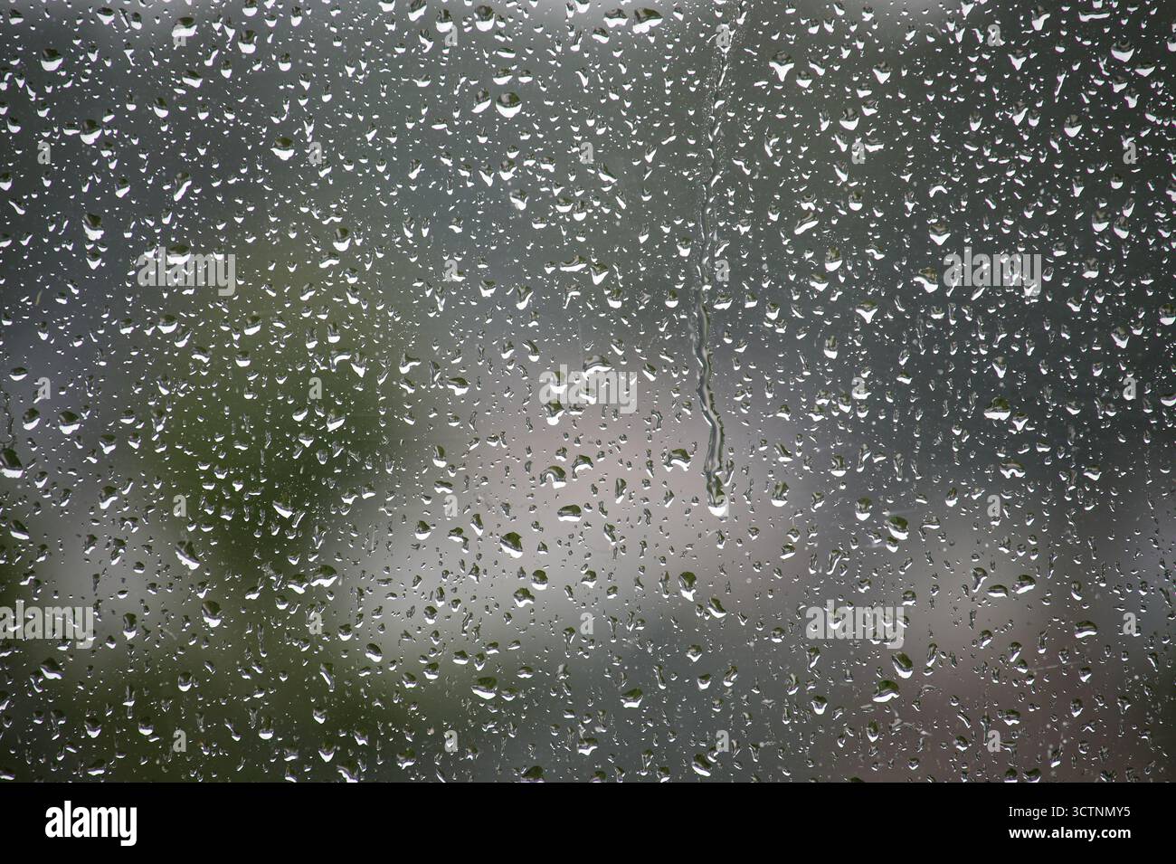 Close-up of raindrops on a window, creating a mesmerizing pattern. Blurred background with hints of nature. Stock Photo