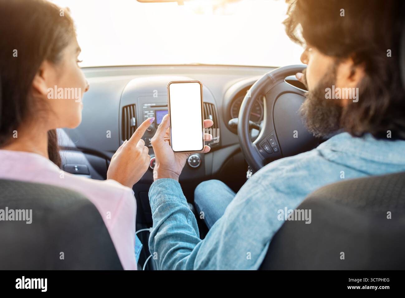 Indian couple using smartphone with blank white screen in car, discussing app Stock Photo