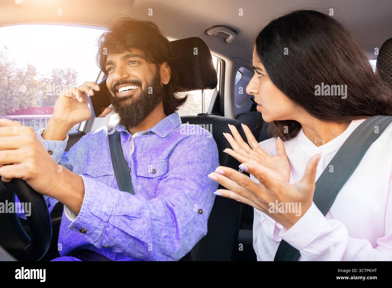 Frustrated Indian woman gesturing while man talks on phone while driving Stock Photo