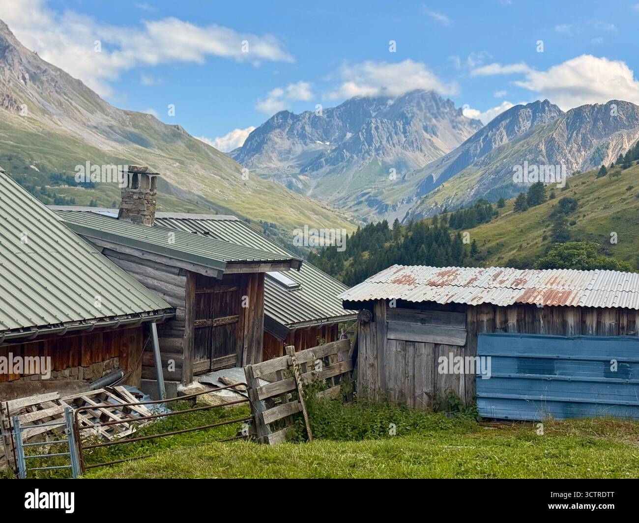 Rustic Wooden Cabins in Alpine Landscape with Forest and Rocky Mountain Peaks under Clear Sky - Smartphone Captured Stock Image