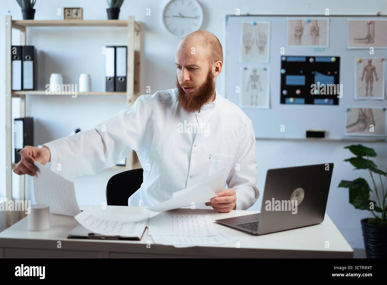 Pensive bearded doctor holding paper, reading medical report in his office. Doctor working in clinic thinking about test results and treatment his pat Stock Photo