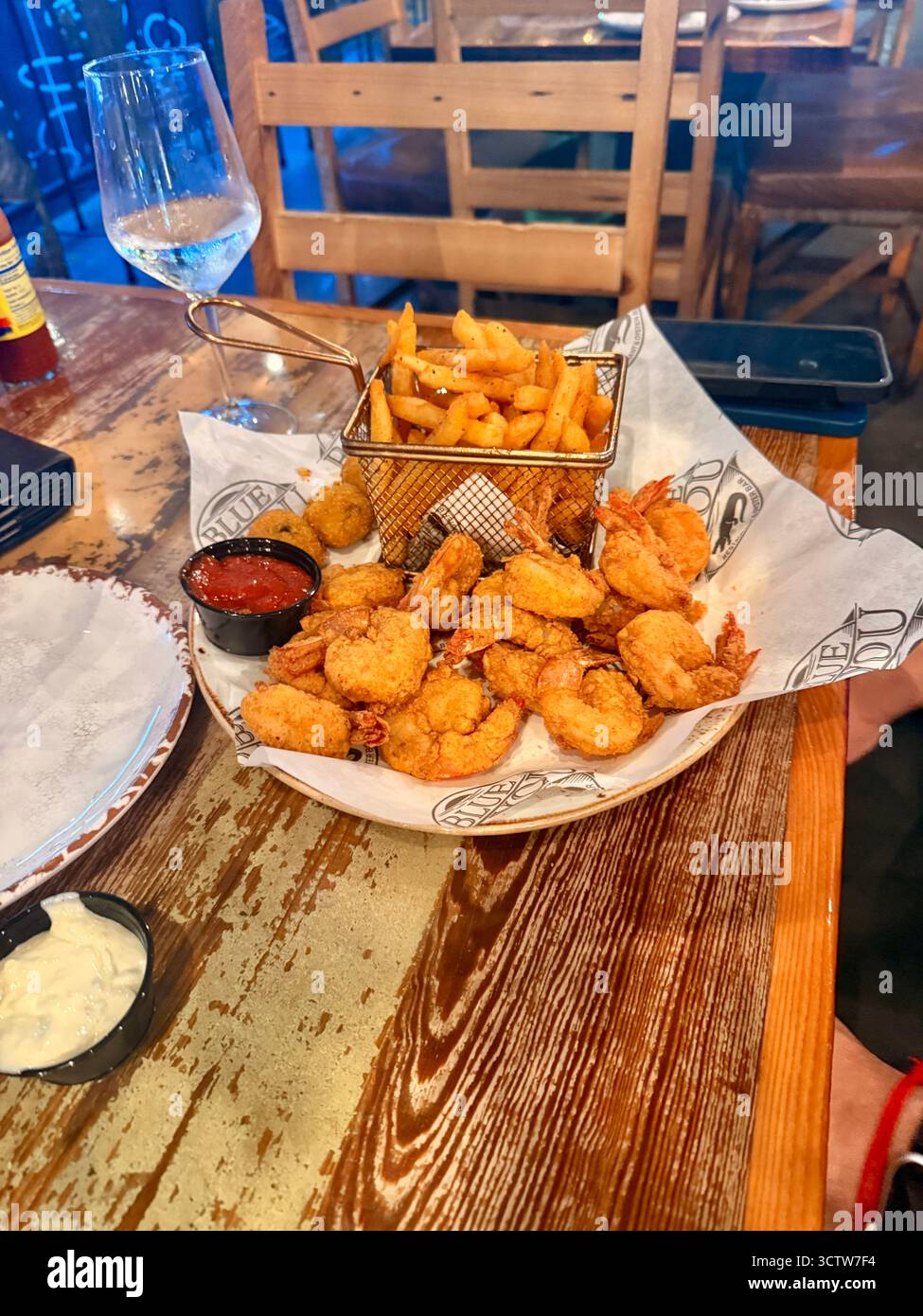 Basket of fried shrimp, chicken tenders and French fries served on a wooden restaurant table in New Orleans, Louisiana, USA, with dipping sauce and a - Smartphone Captured Stock Image
