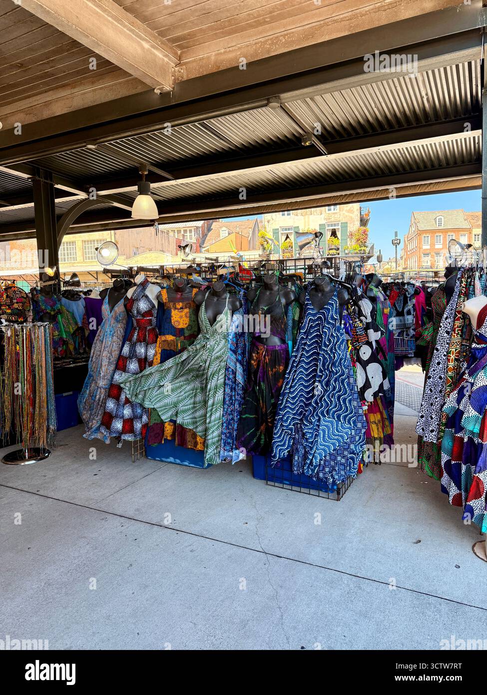 Colorful clothing and fabric items hang from racks at an open-air ...