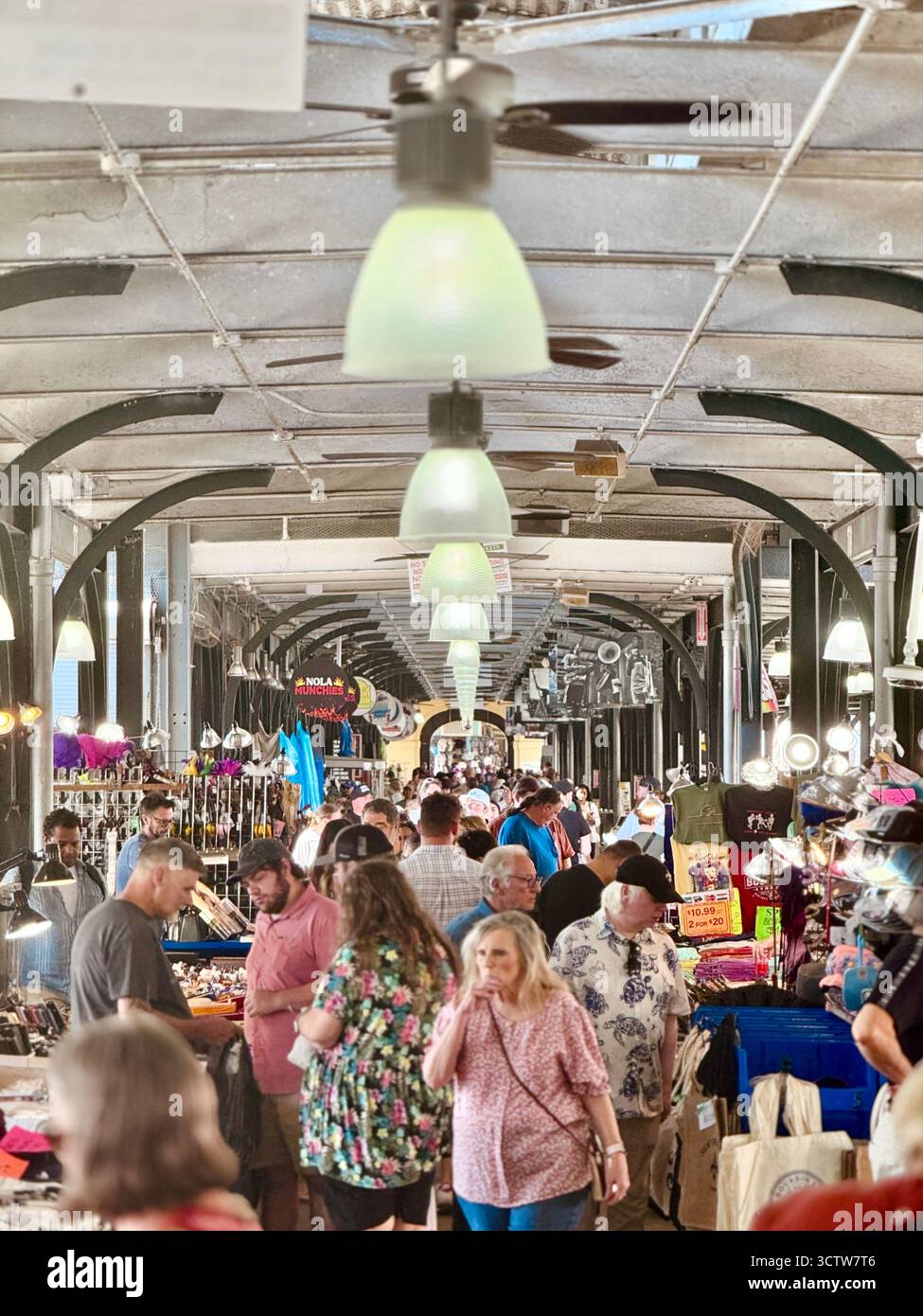 Rows of stalls and vendors line a covered market in New Orleans, Louisiana, USA, with shoppers browsing goods under hanging lights and ceiling fans. - Smartphone Captured Stock Image