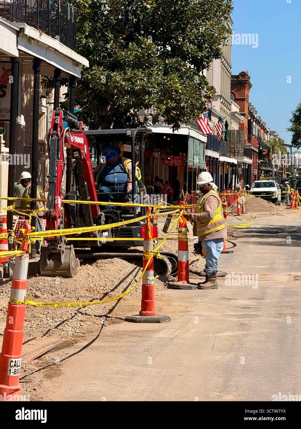 Construction workers and a small excavator repair a street in the French Quarter of New Orleans, Louisiana, USA, with orange cones, caution tape and h - Smartphone Captured Stock Image