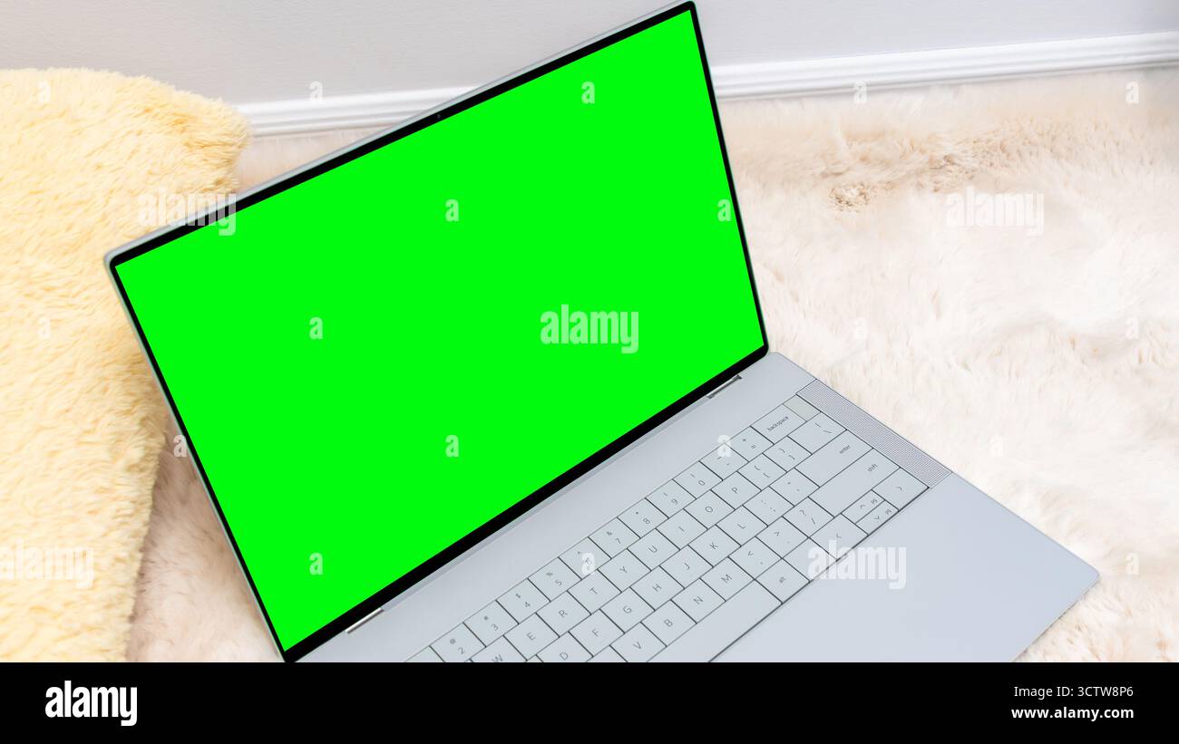 Laptop mock up featuring a vibrant green screen placed on a soft fur rug, ideal for showcasing digital content and creative design projects Stock Photo