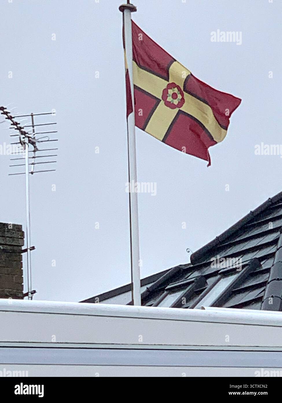 flag of Lancashire England UK British County flying high in the wind on a pole yellow cross red background on a cloth with a rose above a house view - Smartphone Captured Stock Image